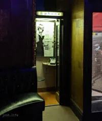 A phone booth inside Blind Pig bar. It has a poster of Audrey Hepburn and has a black landline phone on a small table.